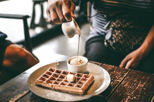 Middelsectie van een man die saus in wafels op tafel in een restaurant giet