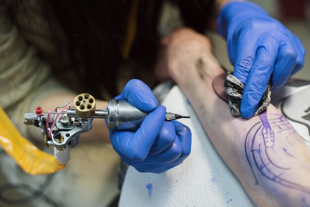 Foto middelsectie van een vrouw die een tatoeage maakt op de hand van een klant.