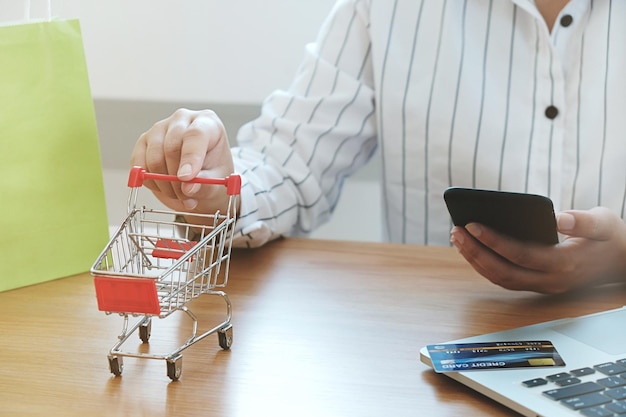 Foto middelsectie van een vrouw die een winkelwagentje vasthoudt terwijl ze een mobiele telefoon op tafel gebruikt