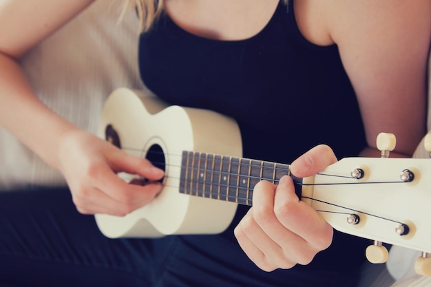 Middelsectie van een vrouw die thuis ukulele speelt