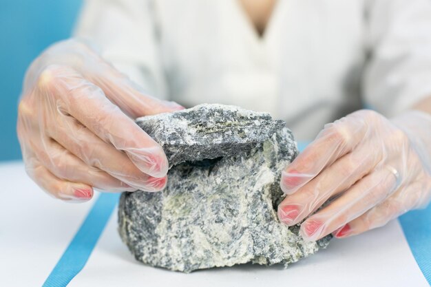 Foto middelsectie van een wetenschapper met handschoenen die asbest vasthoudt aan tafel tegen een blauwe achtergrond