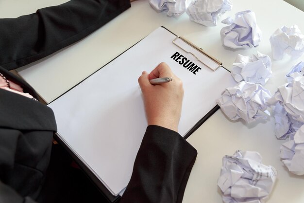 Foto middelsectie van een zakenvrouw die een cv schrijft door verfrommelde papieren aan tafel