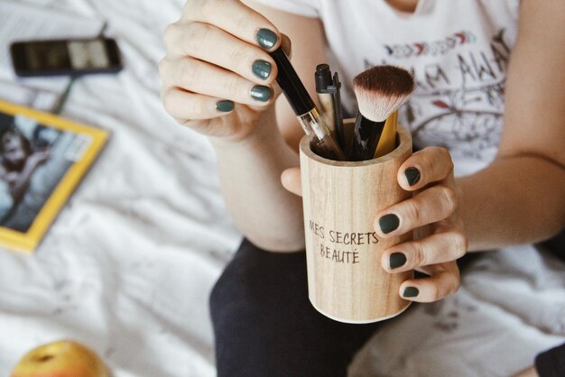 Foto middelsectie van vrouw die een container met make-up vasthoudt terwijl ze thuis op bed zit