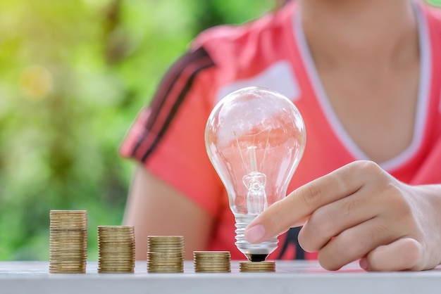 Middelsectie van vrouw met gloeilamp over munten aan tafel