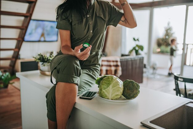 Foto middelsectie van vrouw met groenten bij mobiele telefoon die bij de keukenbank zit