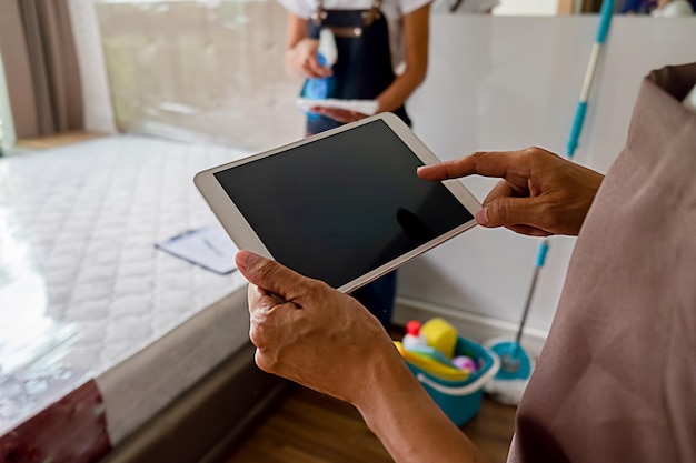 Foto middelsnede van een man die een digitale tablet gebruikt terwijl een vrouw in het ziekenhuis schoonmaakt