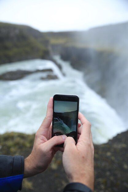 Foto middelsnede van een man die een waterval fotografeert met een smartphone