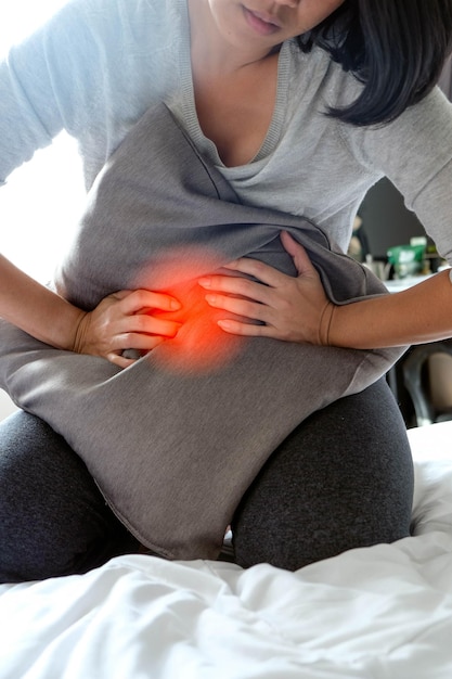 Foto middelsnede van een vrouw die aan pijn lijdt en een kussen vasthoudt terwijl ze op het bed zit