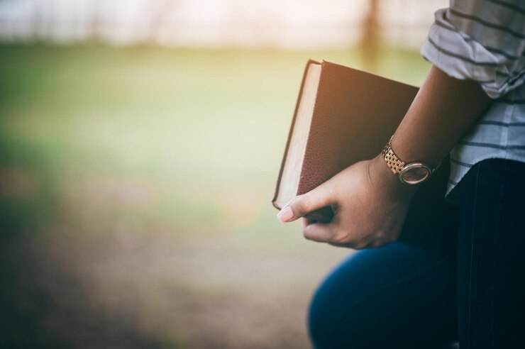 Foto middelsnede van een vrouw die een boek vasthoudt terwijl ze in het park staat