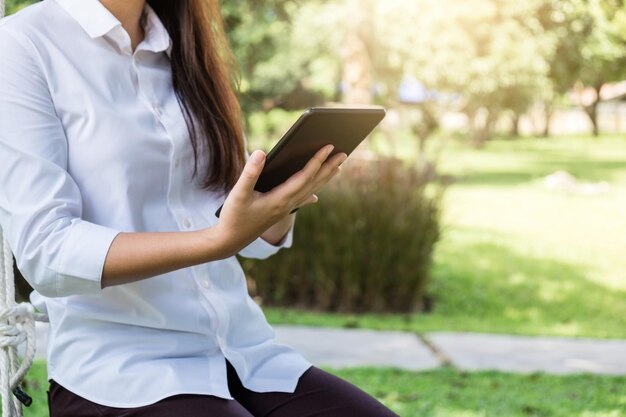 Foto middelsnede van een vrouw die een digitale tablet gebruikt terwijl ze in het park zit