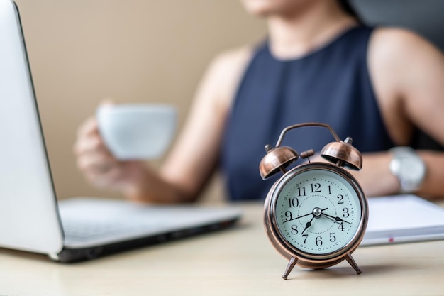 Middelsnede van een vrouw die koffie drinkt terwijl ze een laptop gebruikt bij een klok op tafel