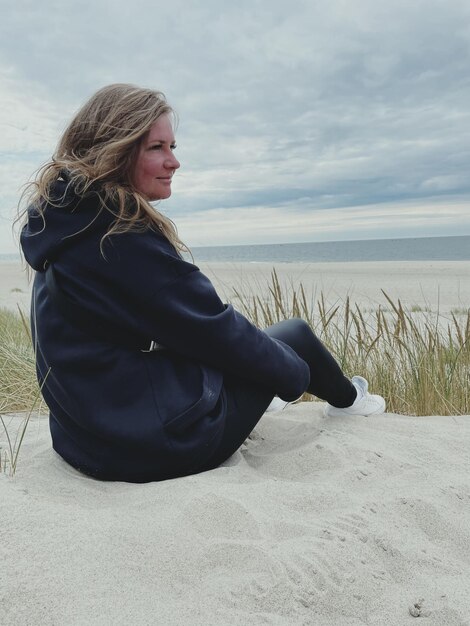 Middelsnede van een vrouw die op het land tegen de lucht zit