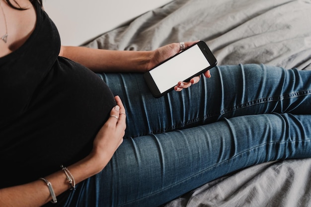 Middelsnede van een vrouw die thuis op het bed zit en een telefoon gebruikt