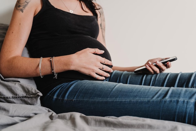 Middelsnede van een vrouw die thuis op het bed zit en een telefoon gebruikt
