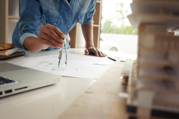 Foto middelsnede van een vrouwelijke architect die een kompas tekent op een blauwdruk aan het bureau