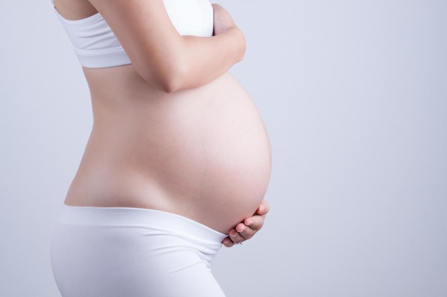 Middelsnede van een zwangere vrouw die de buik aanraakt op een grijze achtergrond