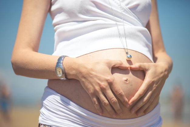 Middelsnede van een zwangere vrouw die een hartvormig teken maakt
