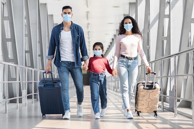 Midden-Oosterse familie van drie die medische maskers dragen die met bagage in luchthaven lopen