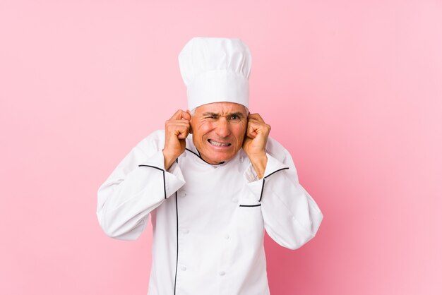 Midden oude geïsoleerde kokmens behandelend oren met handen.