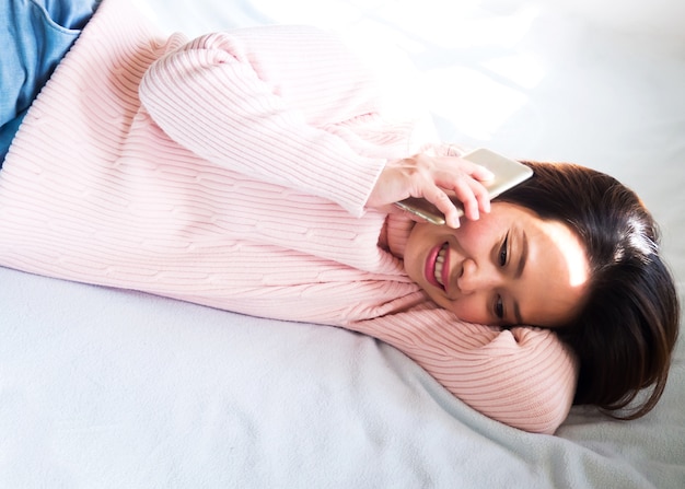 Midden volwassen Aziatische vrouw die op bed bepaalt en mobiele telefoon met behulp van