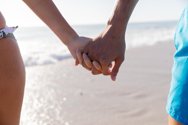 Middendoorsnede van een blank stel dat geniet van de tijd op het strand, wandelend en hand in hand