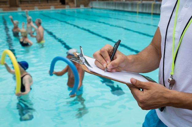 Middengedeelte van zwemcoach die op klembord dichtbij zwembad schrijft