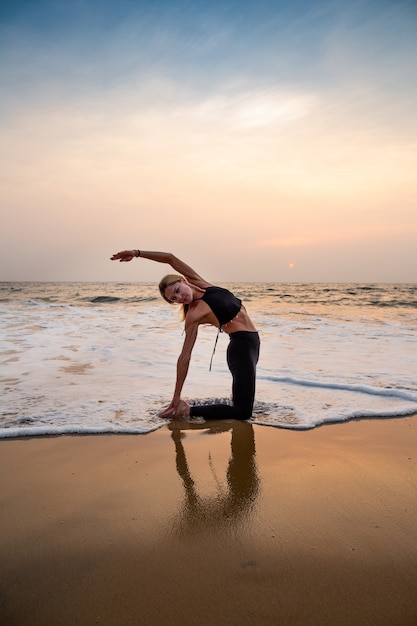 Foto middenleeftijdsvrouw in zwarte het doen van yoga op zandstrand