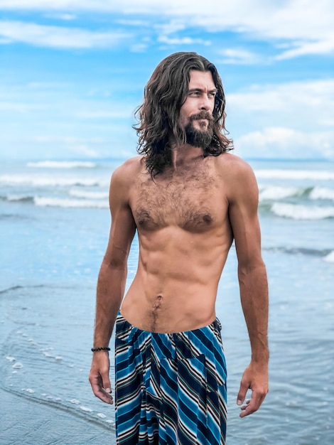 Middenvolwassen shirtloze man die op het strand tegen de lucht staat