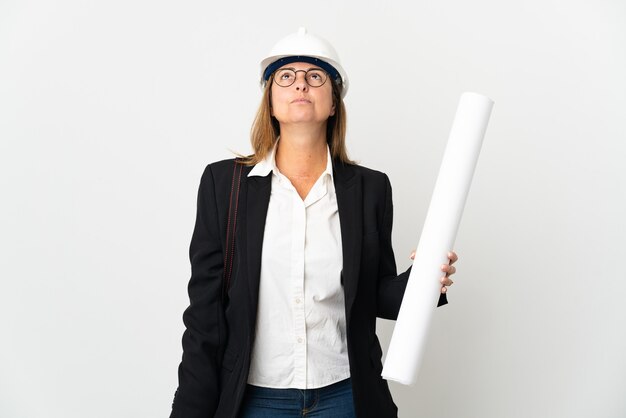 Foto donna dell'architetto di mezza età con il casco e che tiene le cianografie sopra la parete isolata e che osserva in su