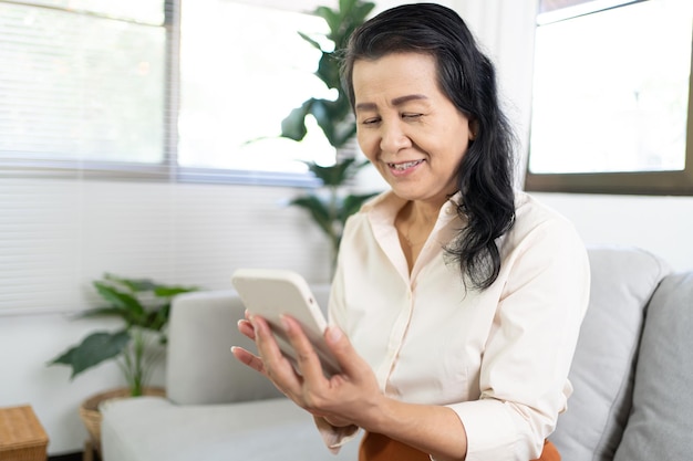 Азиатка средних лет держит мобильный телефон Работает из дома улыбается Красивая зрелая азиатка