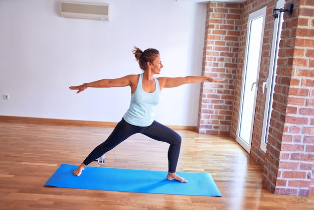 Middle age beautiful sportwoman standing on mat. Practicing yoga doing warrior pose at gym