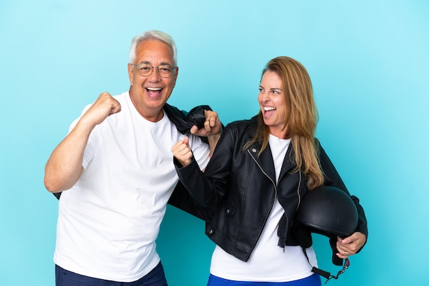 Middle age bikers couple with a motorcycle helmet isolated on blue background celebrating a victory