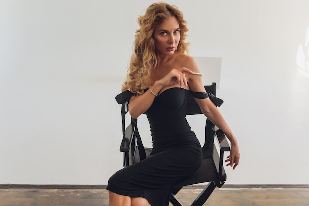 Middle age blond lady in black dress posing on gray background