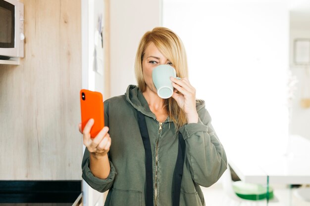 写真 コーヒーを飲み、キッチンでビデオ通話をしている中年の金髪の女性