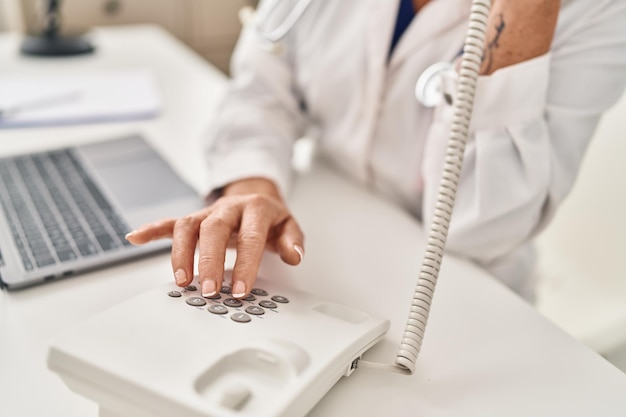 Foto donna bionda di mezza età che indossa l'uniforme del medico che parla al telefono in clinica