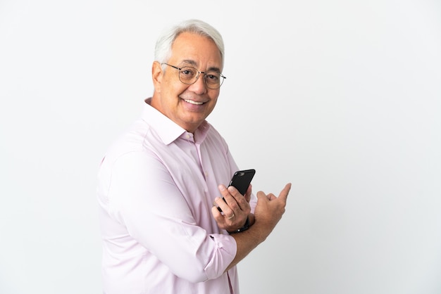 Бразильский мужчина среднего возраста, изолированные на белом фоне, используя мобильный телефон и указывая назад