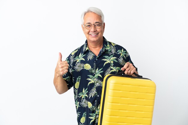Middle age Brazilian man isolated on white background in vacation with travel suitcase and with thumb up