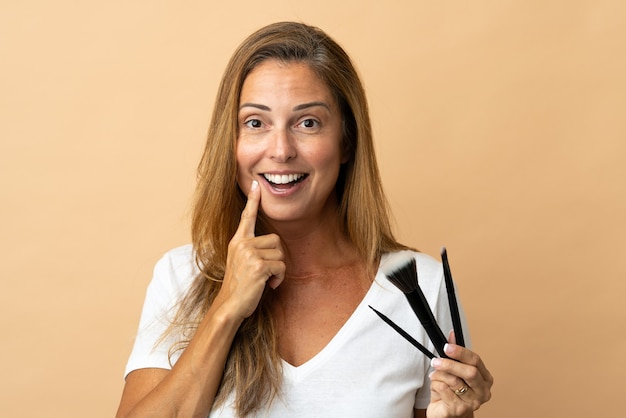 Middle age brazilian woman isolated on beige wall holding makeup brush