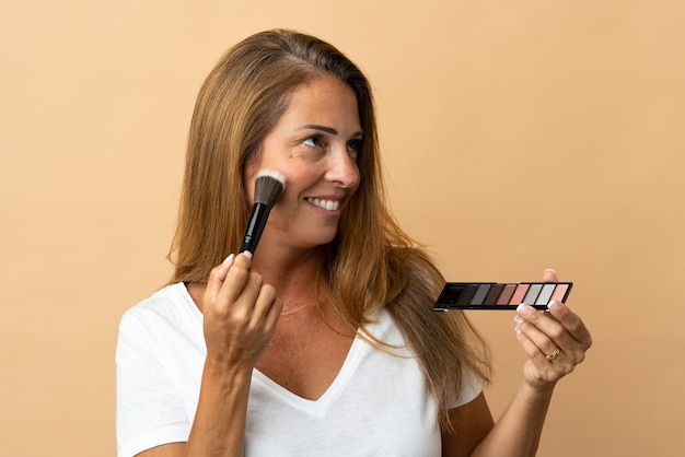 Middle age brazilian woman isolated on beige with makeup palette and happy