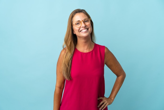 Middle age brazilian woman isolated on blue wall with glasses and happy