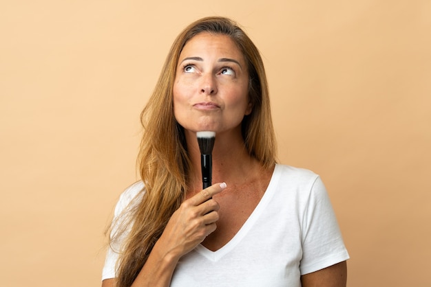 Middle age brazilian woman isolated holding makeup brush and thinking