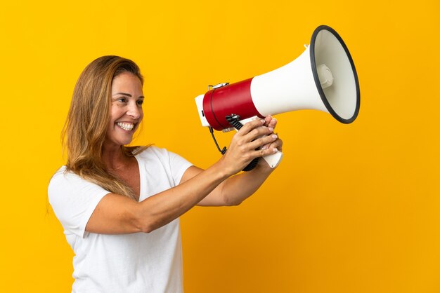 Middle age brazilian woman isolated on yellow wall shouting through a megaphone to announce something