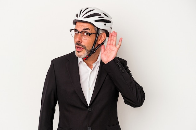 Uomo d'affari di mezza età che indossa un casco da bici isolato su sfondo blu cercando di ascoltare un pettegolezzo.