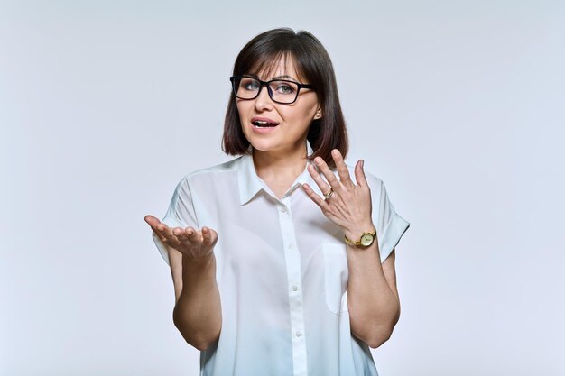 Middle age business woman in glasses talking looking at camera on light background