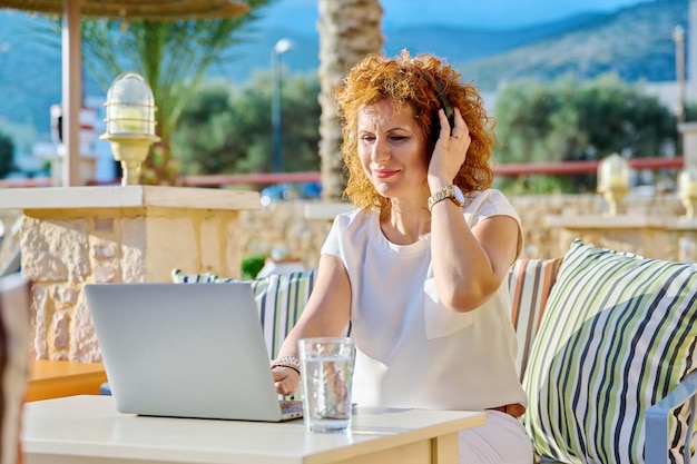 Middle age business woman in headphones using laptop outdoor