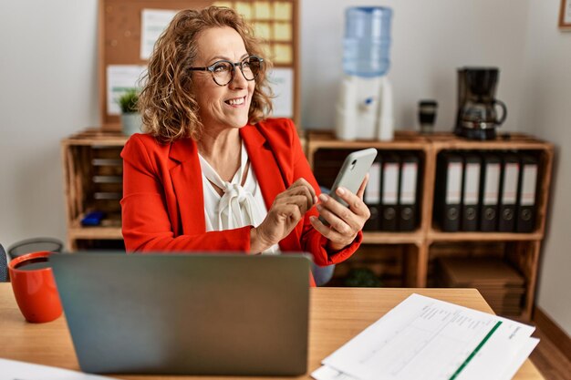 Middle age caucasian businesswoman using laptop and smarphone working at the office