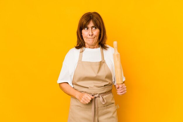 Middle age caucasian cook woman holding a roller isolated confused, feels doubtful and unsure.