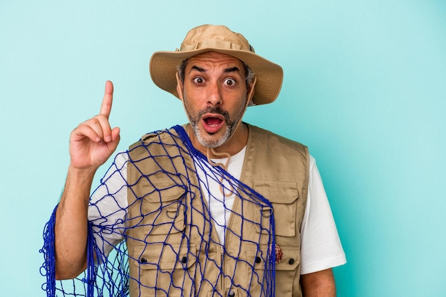 Middle age caucasian fisherman holding net isolated on blue background  having an idea, inspiration concept.