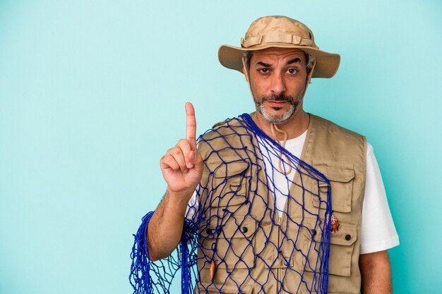 Middle age caucasian fisherman holding net isolated on blue background  showing number one with finger.