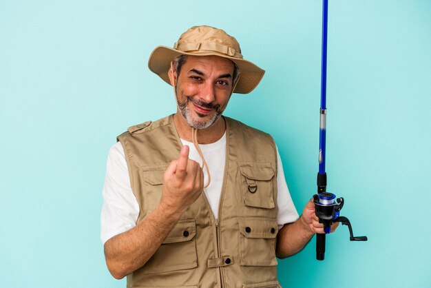 Middle age caucasian fisherman holding rod isolated on blue background pointing with finger at you as if inviting come closer